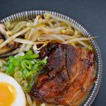 Bol de ramen de shoyu con rodajas de cerdo asado, brotes de bambú, huevo cocido y cebolletas, en un caldo oscuro y brillante