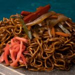 Porción de yakisoba sobre un plato de piedra, con fideos bien dorados y tiras de verduras y beni shoga