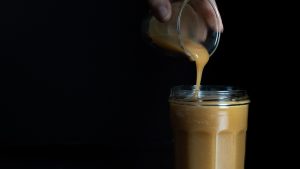 Vertido de salsa de caramelo desde vasito a una jarra transparente, sobre un fondo oscuro