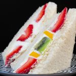 Sándwich sando japonés con frutas y crema, rebanadas de fresa y kiwi entre dos capas de pan de miga esponjoso, en un plato con diseño japonés