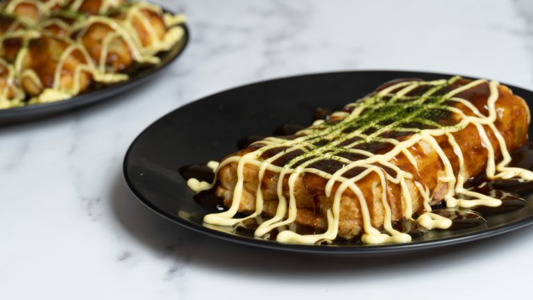 Takoyaki preparado sin sarten especial servido en un plato negro con aderezo de mayonesa y salsa takoyaki, espolvoreado con aonori,